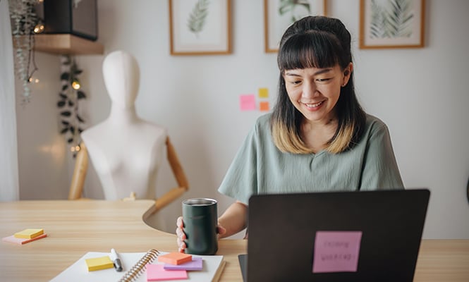 Mujer sentada en un escritorio en un espacio acogedor y organizado, rodeada de decoración.
