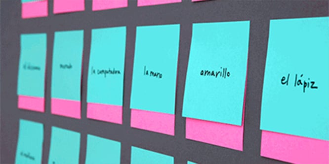 Una pared cubierta con notas Post-it® con palabras en español, utilizadas para practicar el idioma.
