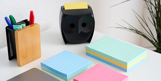 Un escritorio con notas Post-it® de varios colores, un portabolígrafos y un dispensador de notas Post-it® negro con forma de búho.
